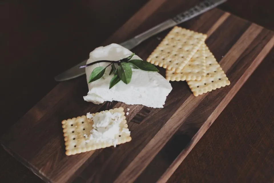 Soft white cheese with crackers on a dark wooden cutting board
